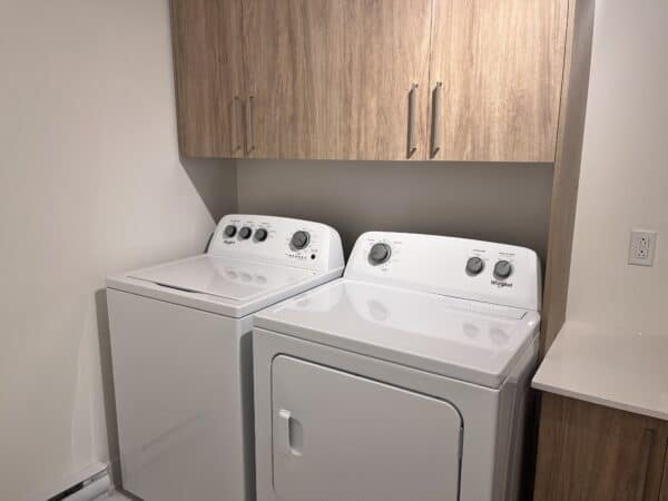 ALT : Coin buanderie avec lave-linge et sèche-linge Blancs, rangements en bois clair, espace optimisé pour gestion immobilière et services de location.