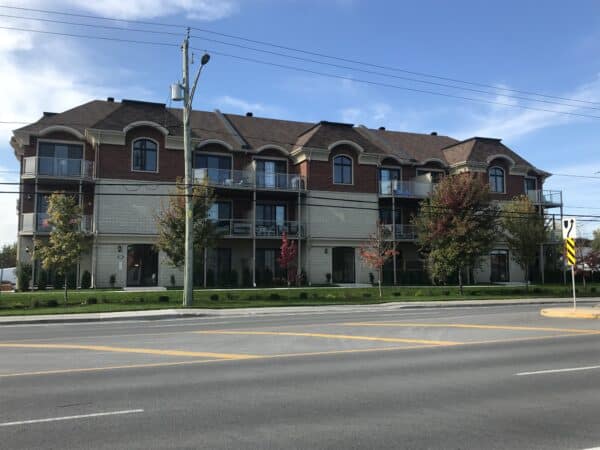ALT : Immeuble résidentiel en gestion avec balcons et espaces verts, situé le long d'une rue animée avec arbres, sous un ciel bleu, illustrant la gestion immobilière professionnelle.