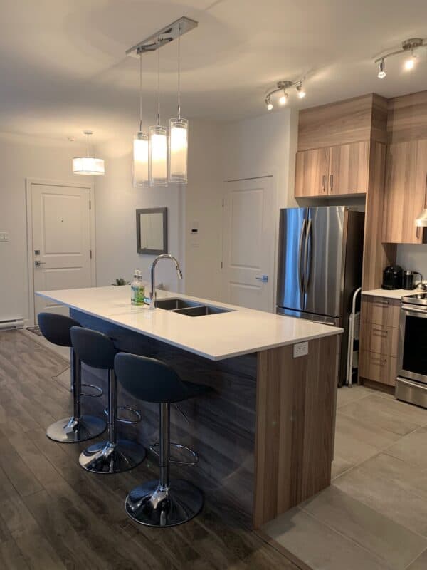 Alt text : Cuisine moderne avec îlot central en marbre, meubles en bois clair, électroménagers en inox et éclairage design, idéale pour gestion immobilière et investissement.