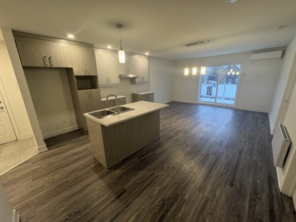 Appartement moderne à Lachute avec cuisine ouverte, espace lumineux, et sol en bois foncé, idéal pour un logement confortable dès maintenant.