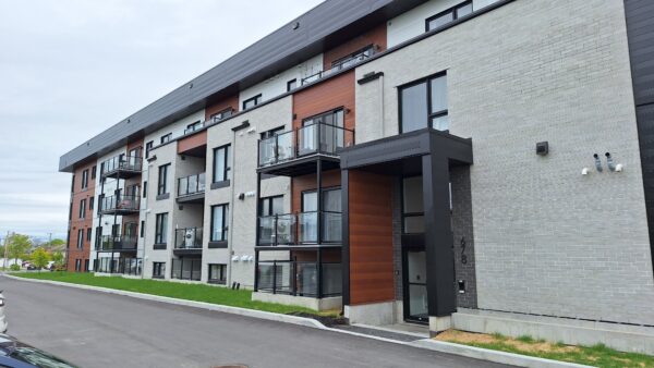 Vue extérieure d'un appartement d'une chambre à Saint-Charles-Borromée, dans un immeuble moderne avec balcons et façade en briques, idéal pour la gestion immobilière.