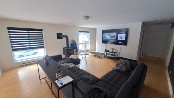 Salon spacieux avec canapé en U, télévision murale, fenêtres lumineuses et cheminée, dans un appartement de 3 chambres à louer à Saint-Calixte, idéal pour famille ou colocation.