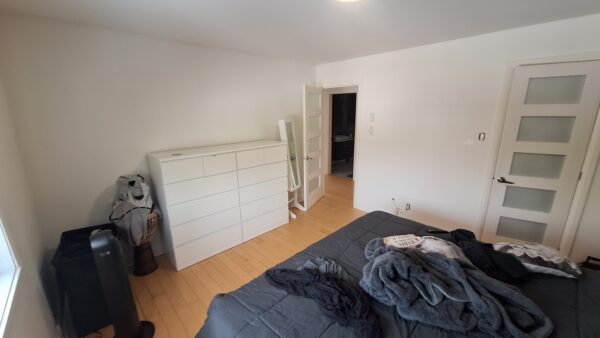 Vue intérieure d'un appartement de 3 chambres à louer à Saint-Calixte, avec un lit, une commode blanche et un espace de vie lumineux, idéal pour une location en juillet.