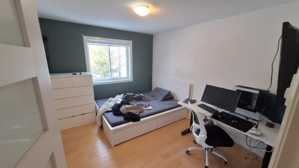 Chambre lumineuse avec lit double, bureau et espace de rangement dans un appartement à louer à Saint-Calixte, idéal pour familles ou professionnels recherchant confort et praticité.