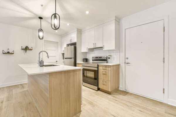 Cuisine moderne avec îlot central, électroménagers en acier inoxydable, et éclairage suspendu dans un appartement de 2 chambres à Saint-Charles-Borromée.