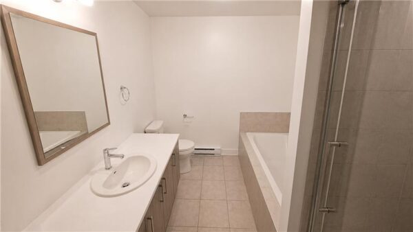 Vue d'une salle de bain moderne avec lavabo, miroir, baignoire et douche dans un appartement à Joliette, disponible pour la gestion immobilière.
