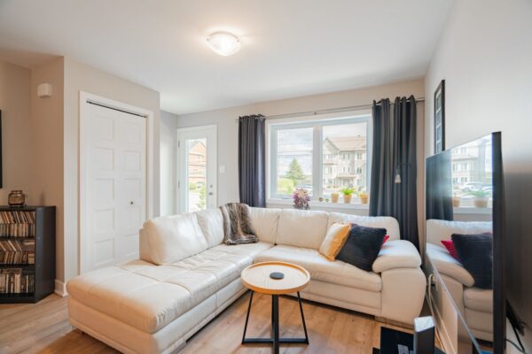 Appartement lumineux avec salon spacieux, grande fenêtre offrant une vue sur le quartier résidentiel de Repentigny, idéal pour la location de logements 2 chambres en juillet.