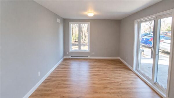 Vue intérieure d'un appartement lumineux avec deux chambres, parquet en bois et grandes fenêtres offrant une vue sur l'extérieur, idéal pour la gestion immobilière.