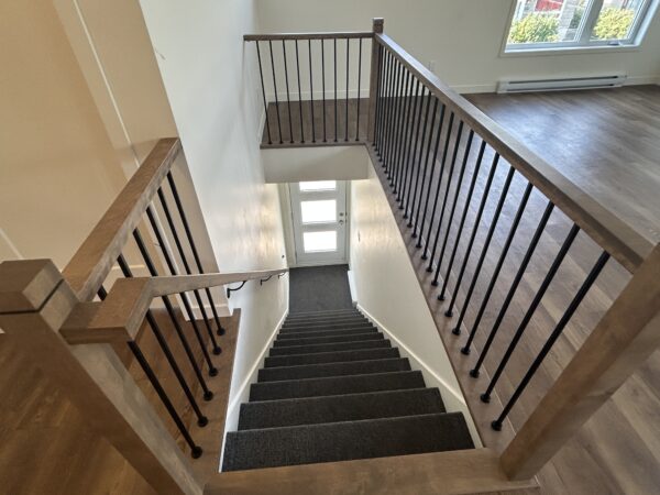 Escalier intérieur avec rampe en bois et balustrade en métal, menant à un étage supérieur lumineux dans un logement à louer à Saint-Jérôme.