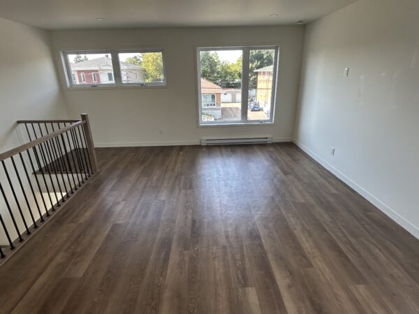 Espace lumineux avec grandes fenêtres dans un appartement de deux chambres à Saint-Jérôme, idéal pour un logement confortable en juillet.