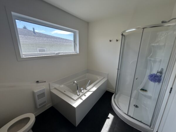 Salle de bain moderne avec baignoire à remous et cabine de douche, lumineuse grâce à une grande fenêtre, idéale pour la gestion immobilière et la location à Saint-Jérôme.