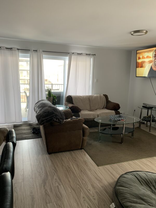 Salon lumineux avec canapé, fauteuils et télévision dans un appartement de Mirabel, idéal pour la gestion immobilière.