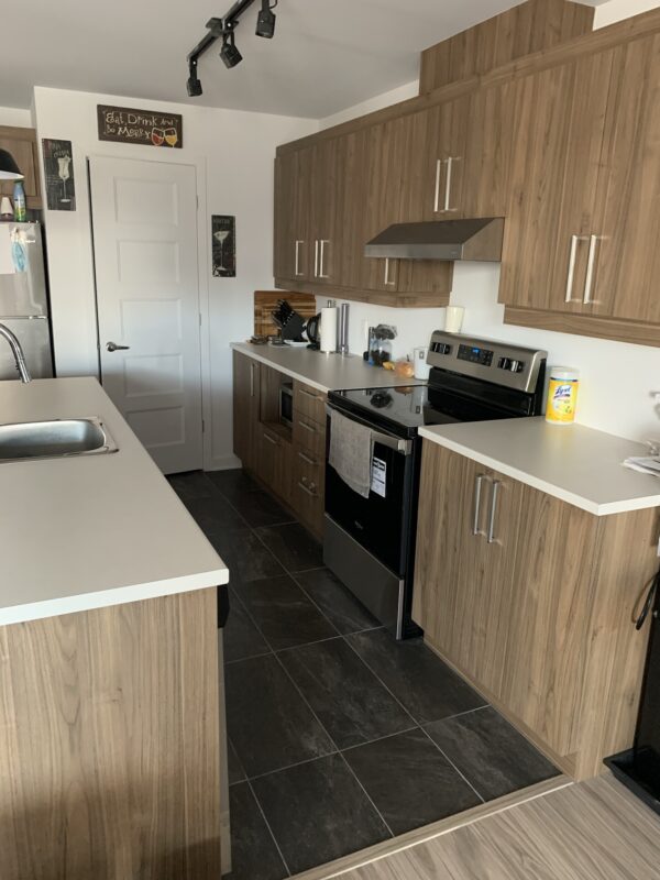 Cuisine d'un appartement 2 chambres à Mirabel, avec armoires en bois, électroménagers modernes, plan de travail spacieux et sol en carrelage noir, idéal pour la gestion immobilière.