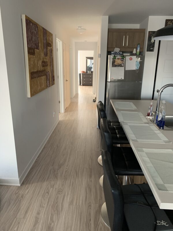 Vue intérieure d'un appartement de deux chambres à Mirabel, avec cuisine moderne, plan de travail, réfrigérateur, et espace salon lumineux, idéal pour la gestion immobilière.