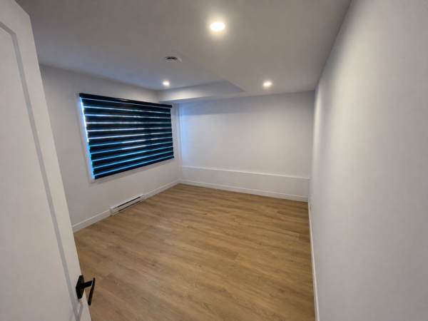 Chambre lumineuse dans un appartement de 3 chambres à Brownsburg-Chatham, avec sol en bois clair, murs blancs et fenêtre à volets roulants modernes.