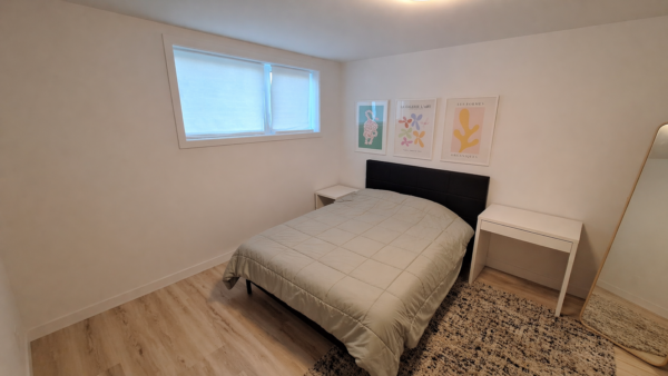 Chambre lumineuse avec lit double, décor moderne et fenêtres offrant une vue dégagée.