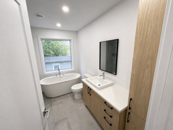 Salle de bain lumineuse avec baignoire, lavabo moderne et rangement, offrant une vue agréable sur le jardin à Brownsburg-Chatham.