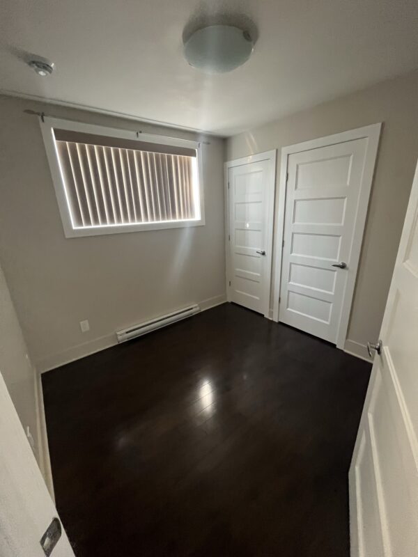 Balcon lumineux avec volets verticaux, intérieur moderne et spacieux, plancher en bois foncé, deux portes de chambre blanches, ambiance chaleureuse et accueillante.